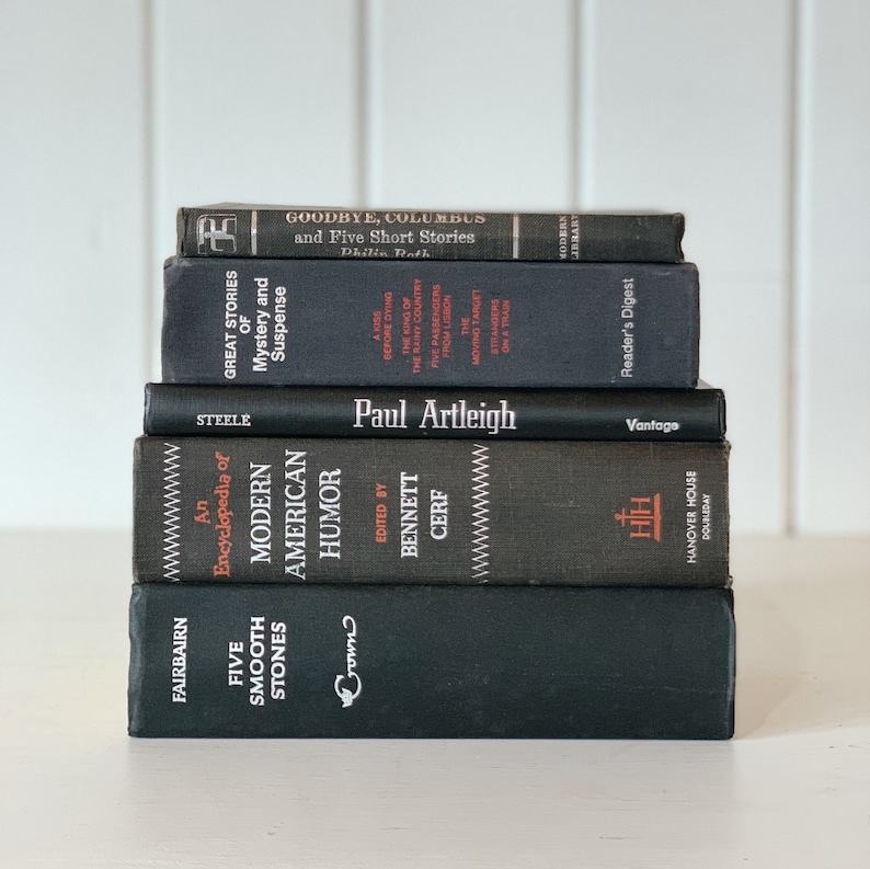 May include: A stack of six vintage books with dark covers. Titles include "Goodbye, Columbus," "Great Stories of Mystery and Suspense," and "Modern American Humor." The books are arranged on a white surface.