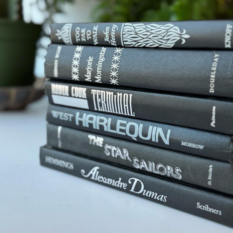May include: A stack of eight black hardcover books with white titles. The titles include "Too Far to Walk", "Morningstar", "Terminal", "Harlequin", "The Star Sailors", and "Alexandre Dumas".