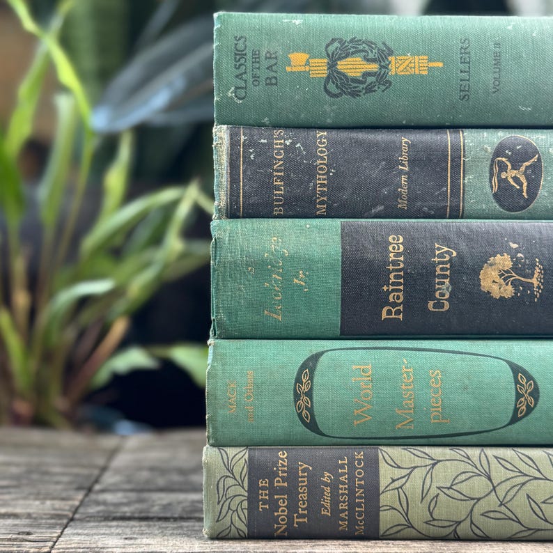 Puede incluir: Una pila de seis libros antiguos con cubiertas verdes y negras. Los t&iacute;tulos incluyen "Classics of the Bar", "Bulfinch's Mythology" y "World Masterpieces". Los libros est&aacute;n dispuestos sobre una superficie de madera, con una planta verde borrosa en el fondo.