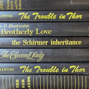May include: A stack of vintage books with black covers and gold lettering. Titles include "The Trouble in Thor," "Brotherly Love," and "The Second Lady." The spines show vertical lines and author names.
