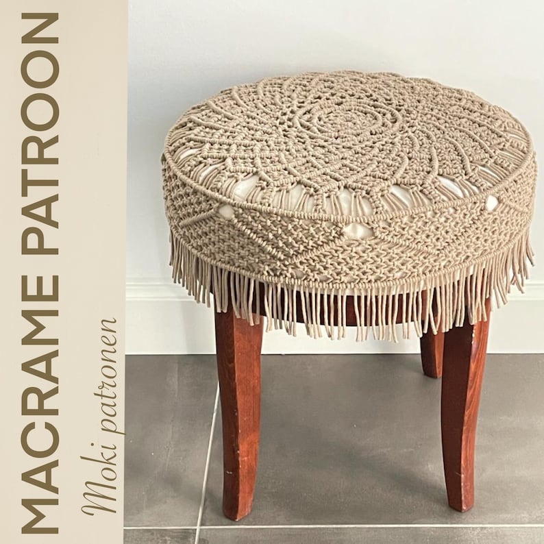 May include: A beige macrame stool cover with a fringe border. The cover is made using a knotting technique and has a circular design. The stool cover is on a wooden stool with four legs.