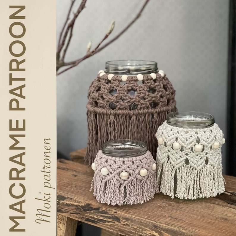 May include: Three macrame candle holders in different sizes, with brown, beige, and light pink cord, and white wooden beads. The candle holders are on a wooden surface.