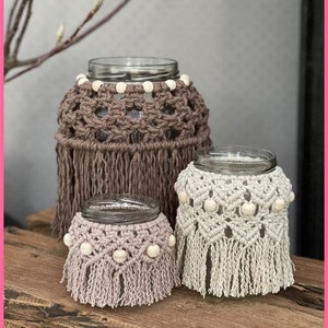 May include: Three glass jars with crocheted covers and white beads. The largest jar has a brown cover with fringe, the medium jar has a white cover with fringe, and the smallest jar has a light pink cover with fringe.