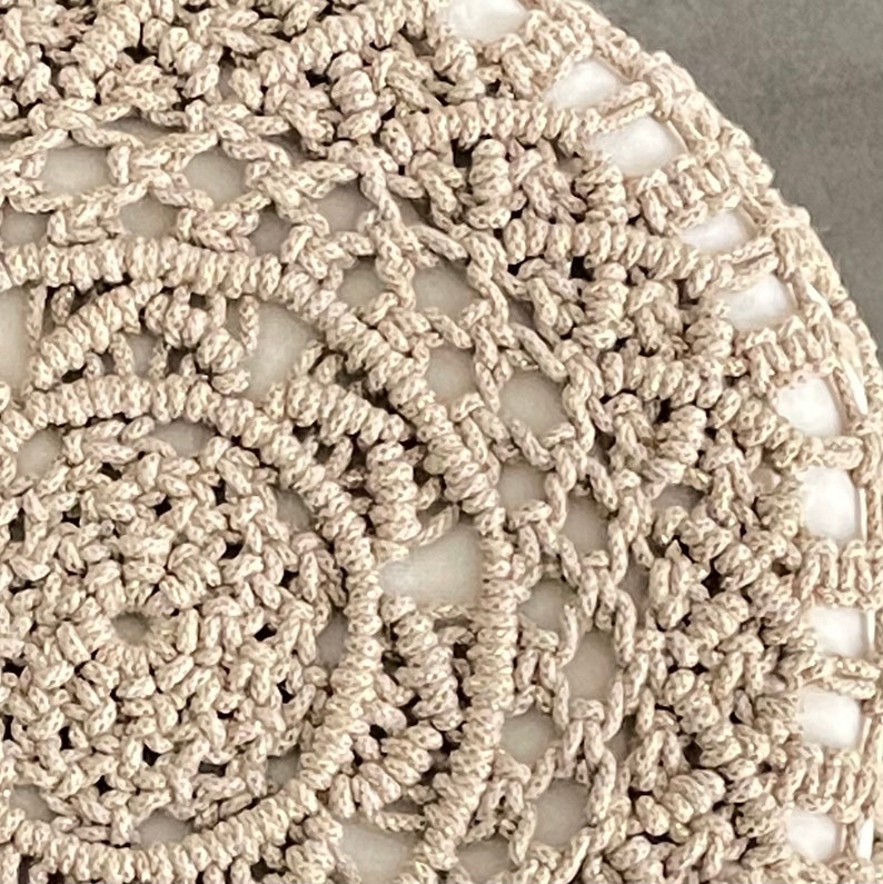 Op de afbeelding: Close-up van een beige rond kussen met een wit centrum.