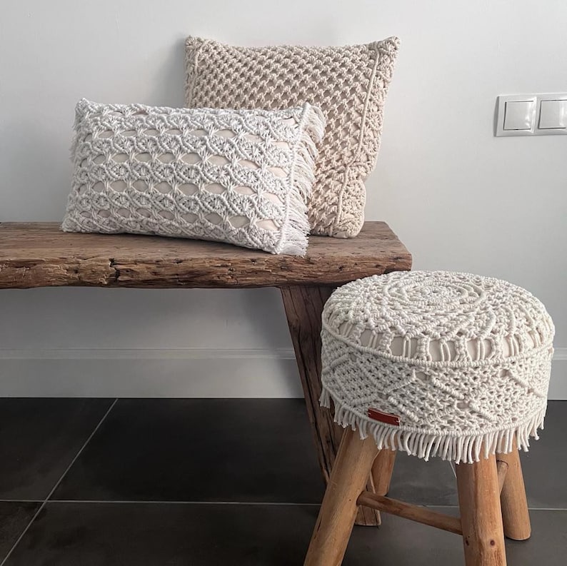 Op de afbeelding: Een houten bank met twee witte gehaakte kussens en een witte gehaakte voetenbank. De bank en de voetenbank hebben een rustieke, natuurlijke uitstraling.