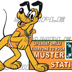 May include: A cartoon dog wearing an orange life vest stands next to a sign that reads "Lifeboat Drill! Everyone to your Muster Station!" The sign is orange with black and white text and a green border. The dog is yellow with black ears and a black nose.