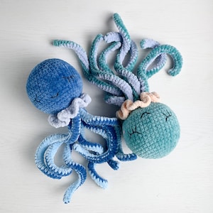 May include: Two crocheted octopus plushies with blue and green yarn. The octopus on the left has a blue body and purple tentacles. The octopus on the right has a green body and pink tentacles.