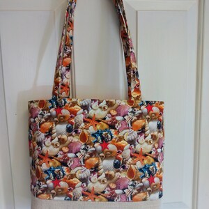 May include: A beige tote bag with a fabric lining featuring a colorful pattern of seashells and starfish.