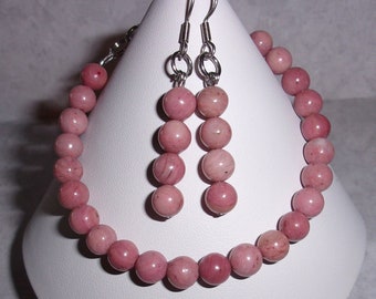 May include: A pink gemstone bracelet and earrings set. The bracelet is made of round, pink beads and the earrings are dangle earrings with pink gemstone beads.