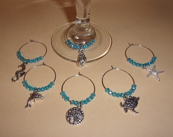May include: Set of six turquoise beaded wine glass charms with silver sea life charms. The charms include a seahorse, dolphin, seashell, starfish, sand dollar, and turtle.