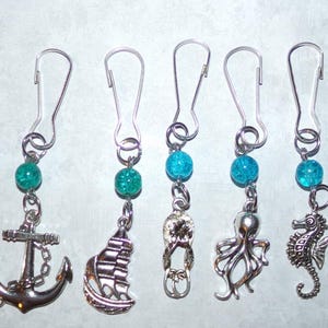 May include: A collection of silver-toned nautical-themed charms, including a ship's wheel, anchor, sailboat, seahorse, octopus, and dolphin. Each charm is attached to a silver clip with a turquoise bead.