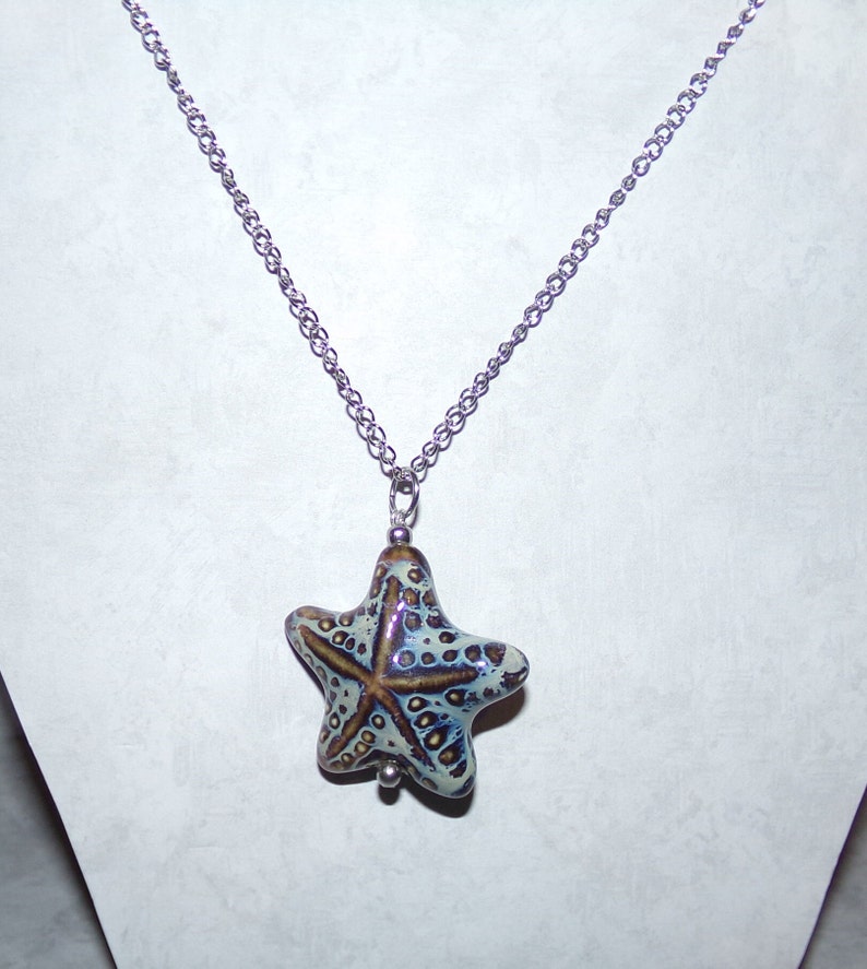 Puede incluir: Un collar de cadena de plata con un colgante de estrella de mar de cer&aacute;mica azul y marr&oacute;n.