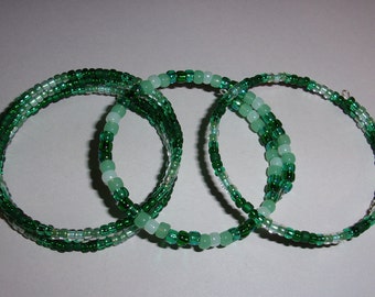 May include: Three green and white beaded bracelets with a gradient of color. The bracelets are made of small, round beads and are stacked on top of each other.