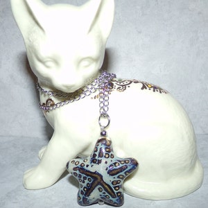 Puede incluir: Un collar de cadena plateada con un colgante de estrella de mar de cer&aacute;mica azul y blanca. El colgante tiene una superficie texturizada con acentos marrones.