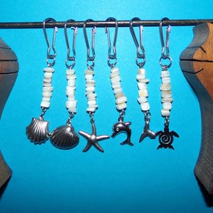 May include: A wooden cat-shaped key holder with six keychains. Each keychain has a silver charm of a seashell, starfish, dolphin, or turtle, and white beads. The key holder is brown and sits against a blue background.