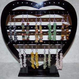 May include: A heart-shaped display stand with 10 pairs of gemstone earrings. The earrings are made with various types of stones, including black, green, brown, and clear.