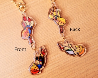May include: Two clear acrylic keychains featuring a cartoon character in a dynamic pose. One side shows the front, the other the back. Each keychain has a gold star-shaped clasp and a gold chain. The character wears red, blue, and yellow clothing.