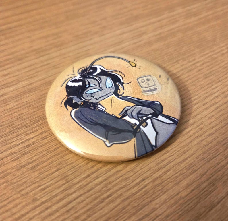 May include: Round button with an illustration of a cartoon character with blue skin, black hair, and a dark suit. The background is a light orange color. The character has a light attached to its head. The button is on a wooden surface.