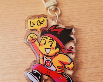 May include: A clear acrylic keychain featuring a cartoon character in a running pose. The character wears a red headband, red pants, and a yellow jacket. The keychain has a metal clasp and the text "LE-GO!" in a yellow speech bubble.