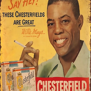Könnte beinhalten: Ein Vintage-Metallschild, das für Chesterfield-Zigaretten wirbt, mit einem Foto von Willie Mays, einem Baseballstar der New York Giants, der sagt: "Say Hey! These Chesterfields are great." Das Schild hat einen roten Hintergrund mit weißem Text und einen gelben Hintergrund mit schwarzem Text. Das Schild zeigt auch eine Packung Chesterfield-Zigaretten.