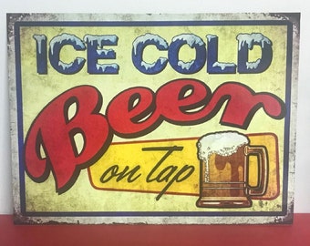 May include: Vintage-style metal sign with a yellow background and blue, red, and white text. The sign reads "ICE COLD Beer on Tap" and features a cartoon illustration of a glass of beer with a frothy head.