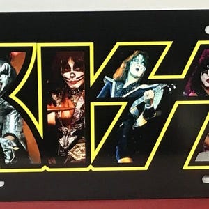 以下が含まれることがあります： 黒い金属製のナンバープレートに、黄色の文字でKISSというバンド名が書かれている。背景は黒。バンドメンバーが文字の中に描かれている。