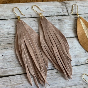 May include: A pair of long, light brown leather fringe earrings with gold hooks.