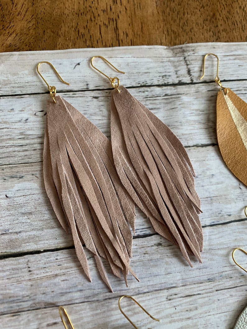 May include: A pair of long, light brown leather fringe earrings with gold hooks.