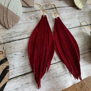 May include: A pair of burgundy leather tassel earrings with gold hooks. The earrings are long and have a fringe design.