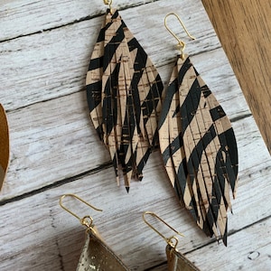 May include: A pair of long, dangling earrings with a black and tan zebra print pattern. The earrings are made of leather and have a gold-tone hook closure.
