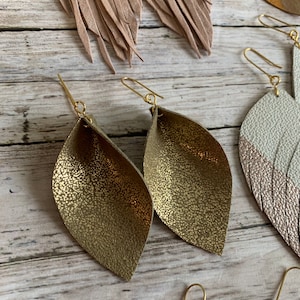 May include: A pair of gold leather earrings with a textured finish. The earrings are shaped like a leaf and have a gold wire hook.