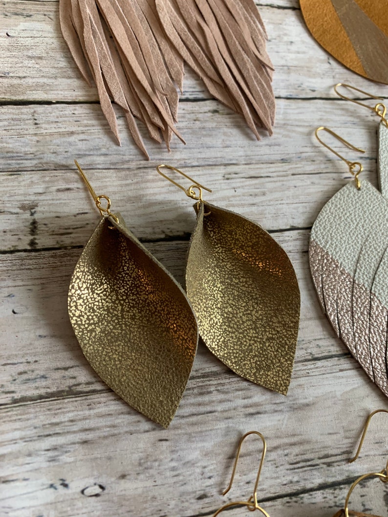 May include: A pair of gold leather earrings with a textured finish. The earrings are shaped like a leaf and have a gold wire hook.