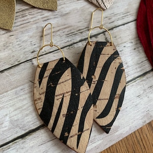 May include: A pair of cork earrings with a black and white zebra print. The earrings are shaped like a teardrop and have gold hooks.