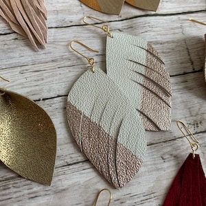May include: A pair of gold tone earrings with a white and rose gold leather feather design.