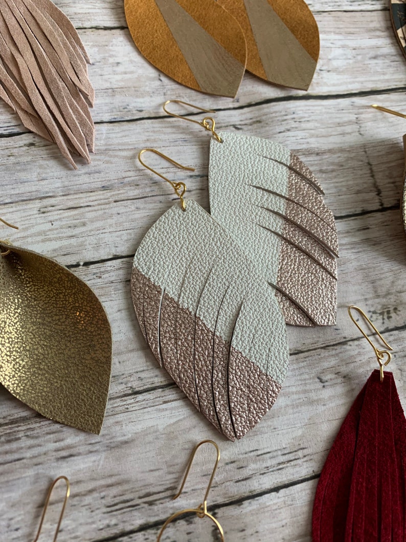 May include: A pair of gold tone earrings with a white and rose gold leather feather design.
