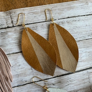 May include: A pair of gold leaf earrings with a brown and beige striped design. The earrings are made of leather and have a simple gold hook closure.