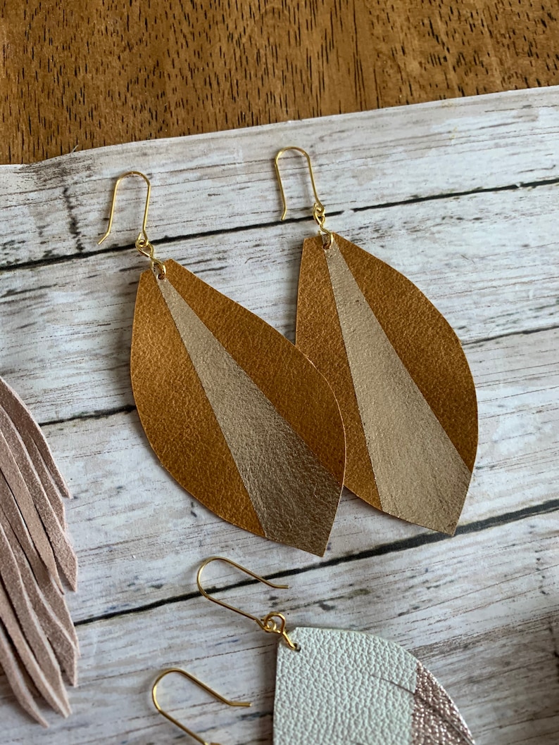 May include: A pair of gold leaf earrings with a brown and beige striped design. The earrings are made of leather and have a simple gold hook closure.