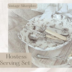 May include: A vintage silverplate hostess serving set. The set includes serving utensils and a floral patterned serving bowl. The utensils are silver with cream-colored handles. The bowl and utensils are arranged on a wooden serving tray.