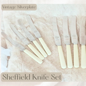 May include: A set of vintage silverplate knives with cream-colored handles. The blades are silver and the handles are a light cream color. The text "Vintage Silverplate" and "Sheffield Knife Set" are visible.
