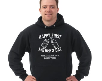 May include: Black hooded sweatshirt with the text "Happy First Father's Day" in white. The graphic includes a baby bottle and a beer bottle. Below the text are the names Kayla, Mandy, Dani, Bobbi, and Trina.