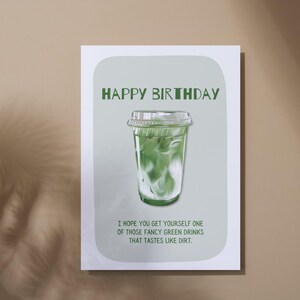 May include: A birthday greeting card with a green and white illustration of a green drink in a clear plastic cup. The text "HAPPY BIRTHDAY" is at the top, with a humorous message below.