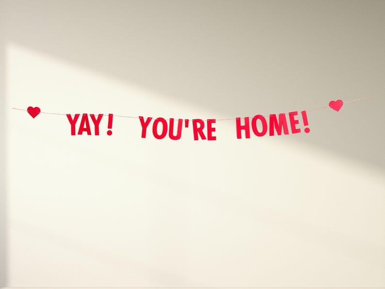 Pode incluir: Faixa de papel vermelha com o texto "YAY! YOU'RE HOME!" e recortes de cora&ccedil;&otilde;es vermelhos em cada extremidade.