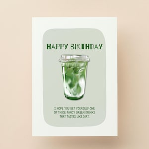 May include: A greeting card with the words "HAPPY BIRTHDAY" in green. The card features an illustration of a green drink in a clear plastic cup. The text below reads, "I HOPE YOU GET YOURSELF ONE OF THOSE FANCY GREEN DRINKS THAT TASTES LIKE DIRT."