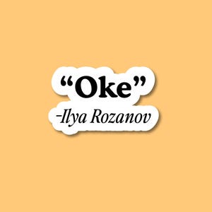 May include: A sticker with the word "Oke" in bold black font, enclosed in a white cloud-shaped border. Below the word is the name "-Ilya Rozanov" in a smaller, italicized black font. The background is a solid shade of orange.