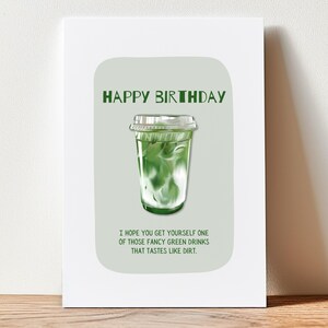 May include: Greeting card with a green and white matcha drink illustration. The text "HAPPY BIRTHDAY" is at the top, with the message "I HOPE YOU GET YOURSELF ONE OF THOSE FANCY GREEN DRINKS THAT TASTES LIKE DIRT." below.