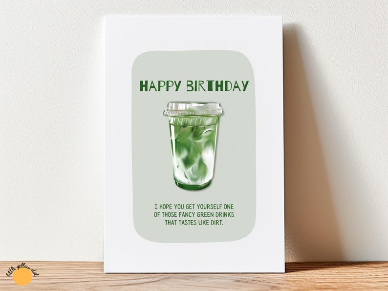 May include: Greeting card with a green and white matcha drink illustration. The text "HAPPY BIRTHDAY" is at the top, with the message "I HOPE YOU GET YOURSELF ONE OF THOSE FANCY GREEN DRINKS THAT TASTES LIKE DIRT." below.