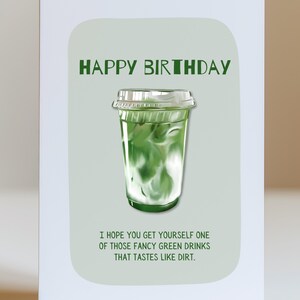 May include: A birthday greeting card with a green and white drink illustration. The words "HAPPY BIRTHDAY" are at the top, with the text "I HOPE YOU GET YOURSELF ONE OF THOSE FANCY GREEN DRINKS THAT TASTES LIKE DIRT." below the drink.