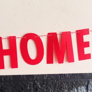 Pode incluir: Faixa de papel vermelha com a palavra "HOME!" enfiada em um barbante branco.