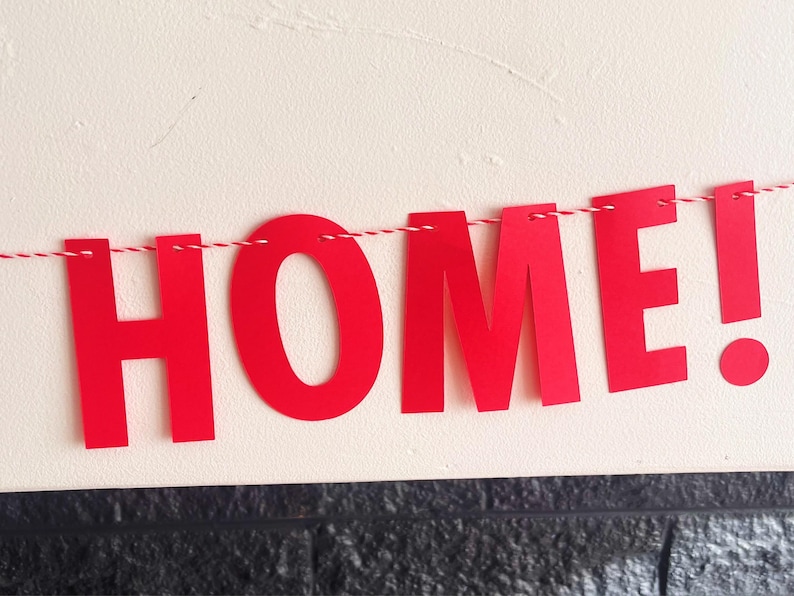 Pode incluir: Faixa de papel vermelha com a palavra "HOME!" enfiada em um barbante branco.