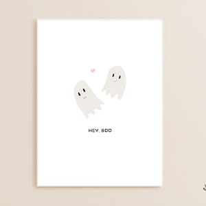 Può includere: Una stampa artistica bianca con un design minimalista raffigurante due fantasmi dei cartoni animati sorridenti e un piccolo cuore rosa. Il testo "HEY. BOO" è stampato sotto i fantasmi. Adatta per Halloween.